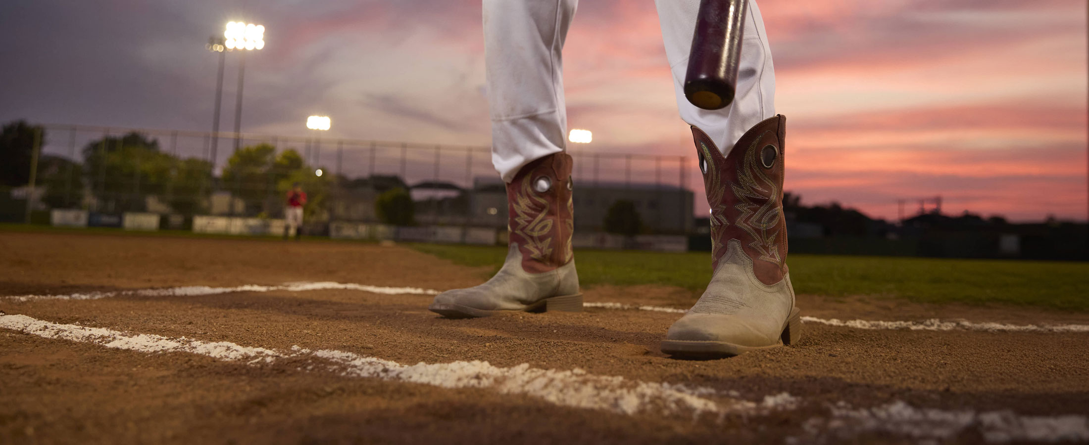 A man wearing Justin untamed western boots in red and grey while standing on a baseball field.